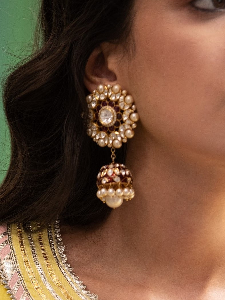 Featuring a pair of 18kt Gold plated red enameled jhumkis studded with vellore polki along with pearl drops set in 92.5 Silver