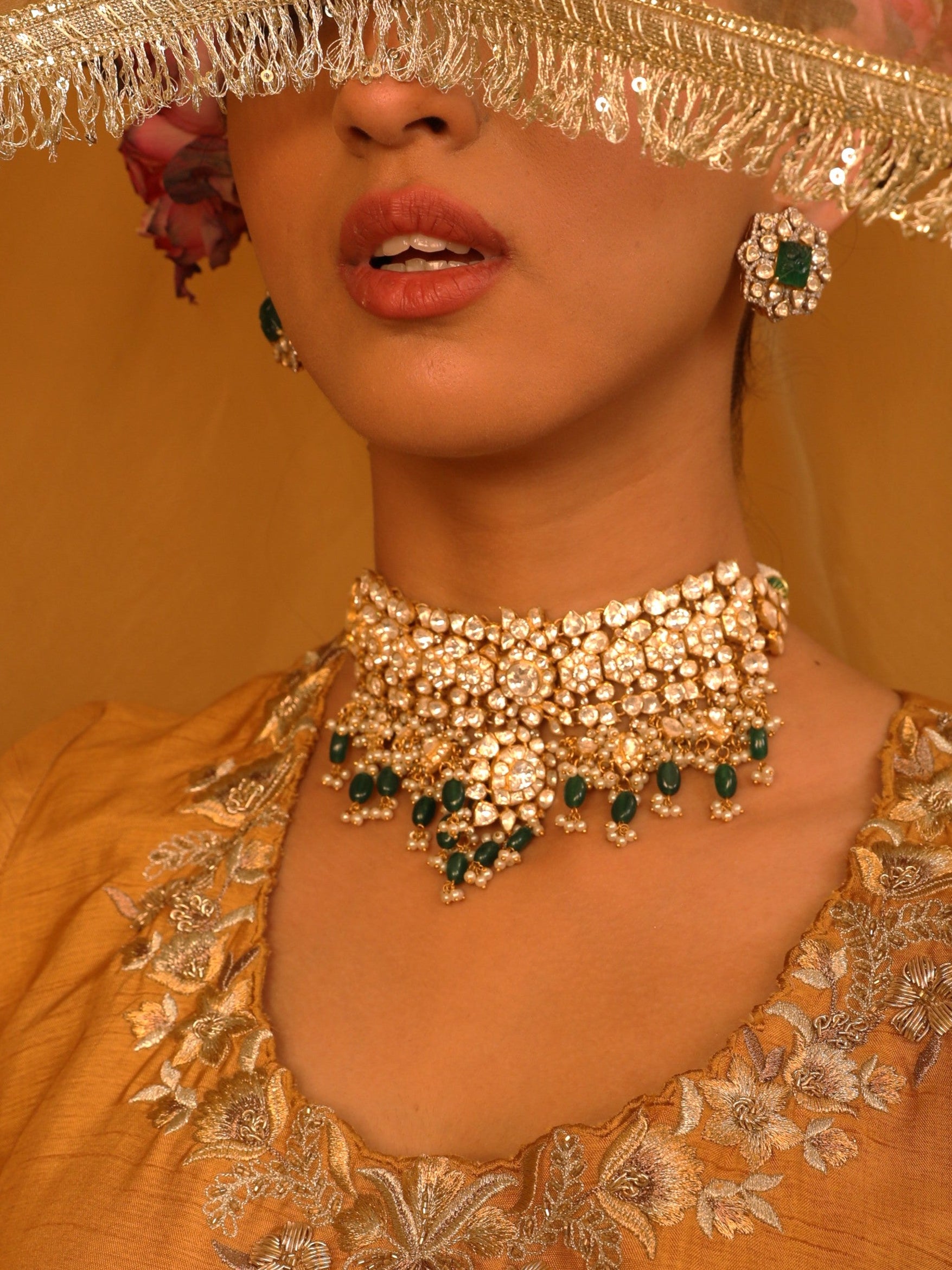 Woman wearing gold jewelry with green stones against a yellow background