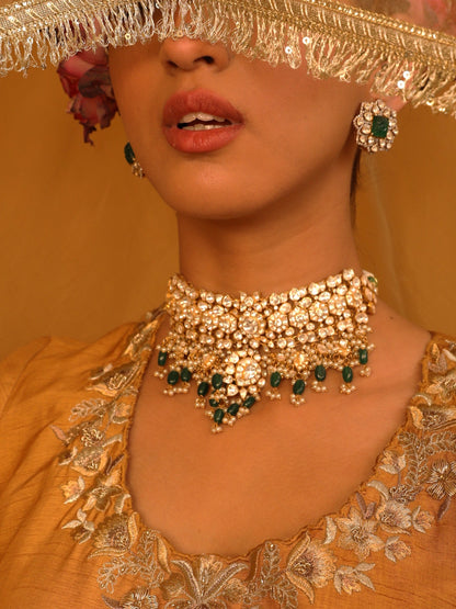 Woman wearing gold jewelry with green stones against a yellow background