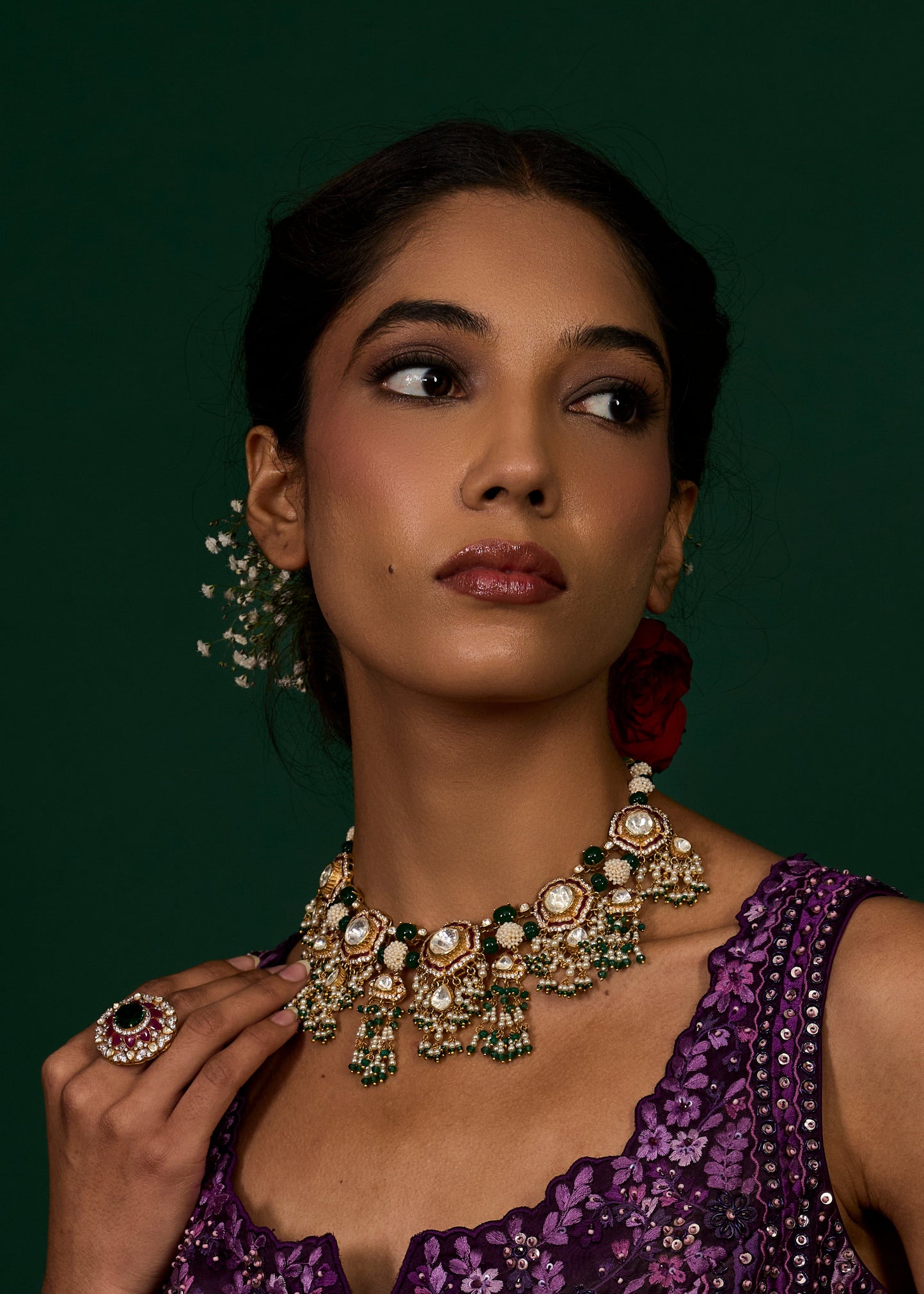 Woman wearing a purple dress with gold jewelry against a dark green background