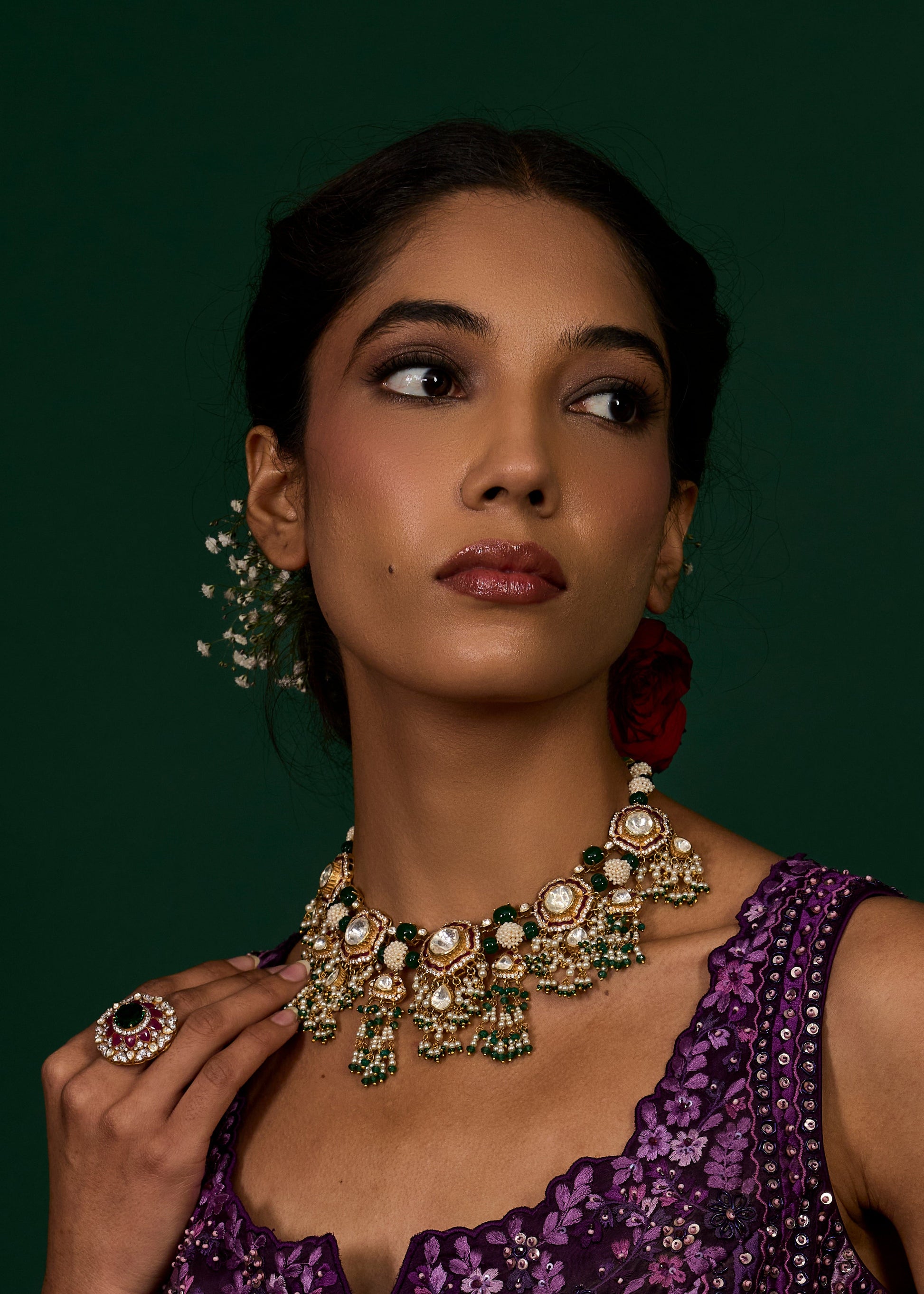 Woman wearing a purple dress with gold jewelry against a dark green background