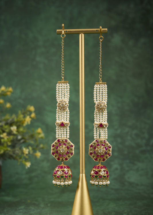 Ornate earrings with pearl and gemstone details on a gold stand against a green background.